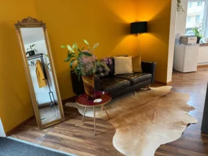 Wartebereich mit gemütlicher Couch, Spiegel und Pflanzen im AINHOA BEAUTY-WERK